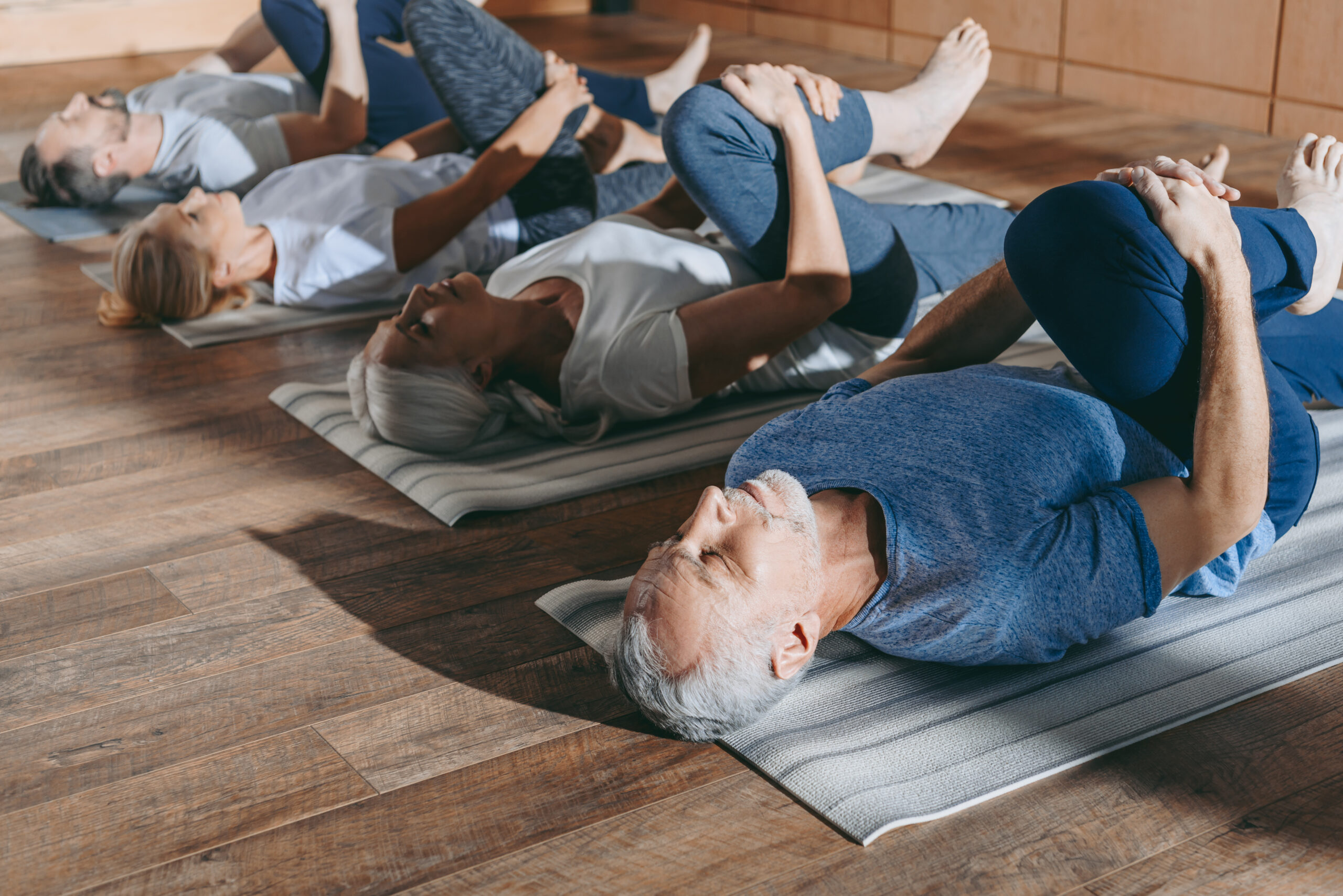 Grupa seniorów wykonuje ćwiczenia rozciągające z jogi
